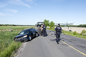 A man in a uniform holds a bicycle next to a car that in a ditch