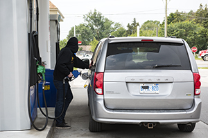 A man in a black hoodie pumps gas into a van with a shrouded license plate